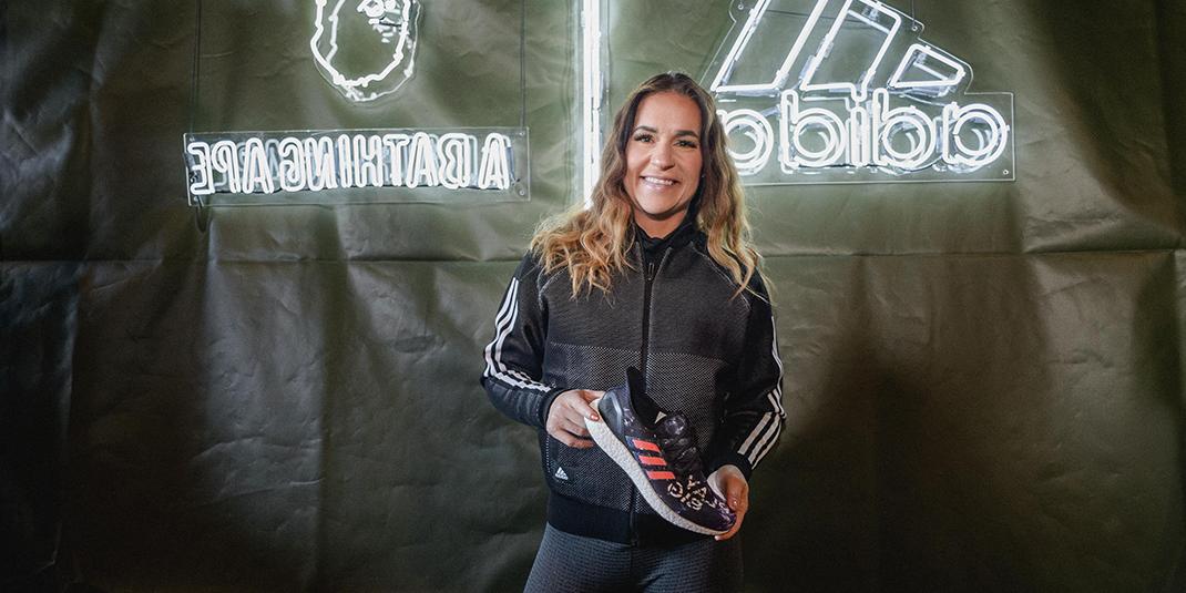 Jen Welter holding a sneaker in front of a banner that says Adidas